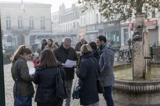 Town square in Val-d'Oise at dawn with residents and business owners discussing municipal papers, natural diffuse light, authentic local atmosphere.