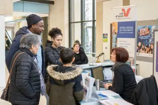 Residents in a public building in the Val-d'Oise, talking with a staff member at an information desk, natural daylight and authentic local atmosphere